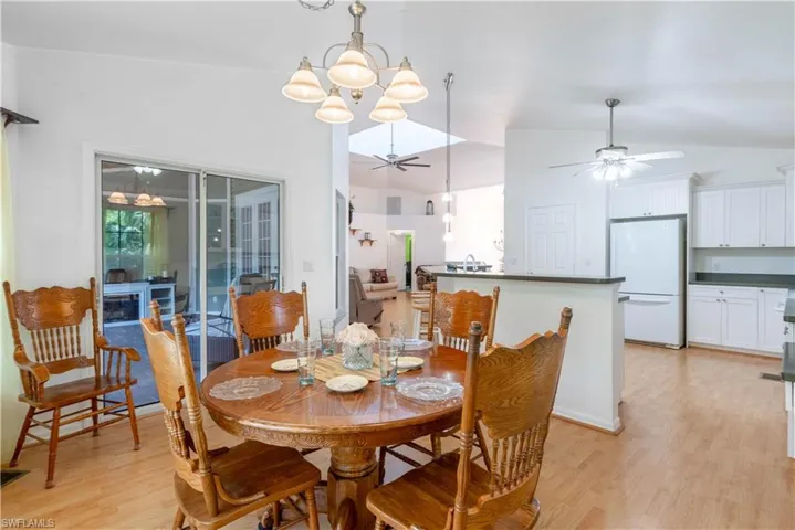 Dining area with vaulted ceiling, ceiling fan with notable chandelier, and light hardwood / wood-style flooring