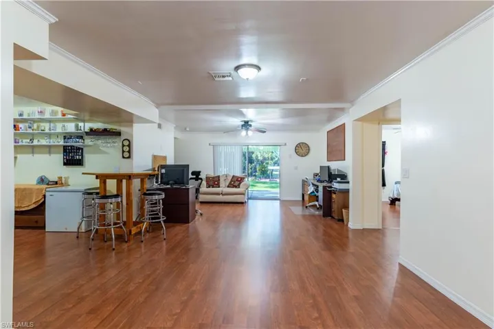 Living room with hardwood / wood-style flooring, ceiling fan, indoor bar, and ornamental molding