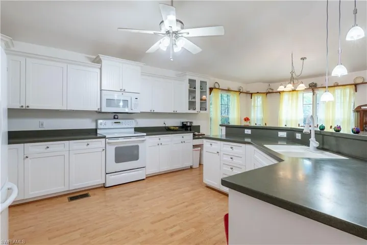 Kitchen featuring hanging light fixtures, white appliances, sink, and white cabinets