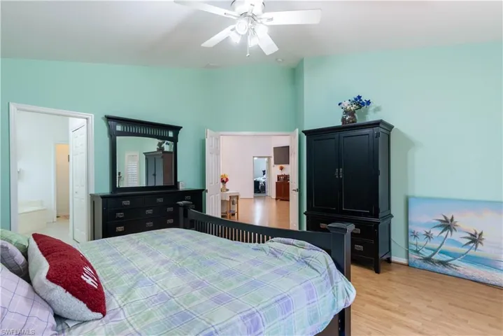 Bedroom with light wood-type flooring, ensuite bath, lofted ceiling, and ceiling fan