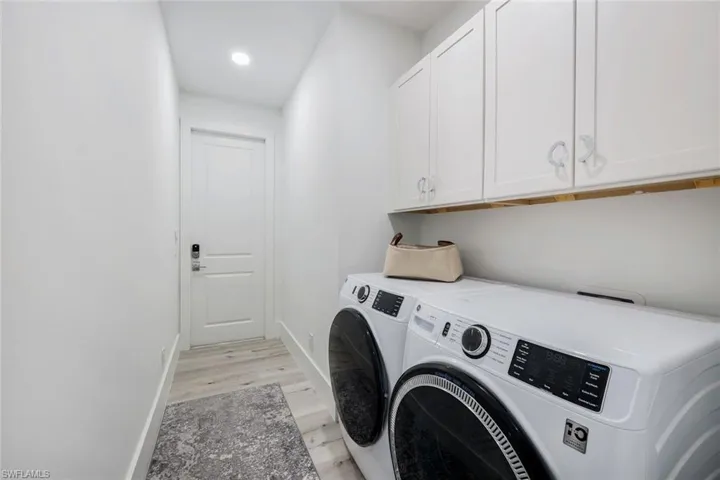 Washroom with light hardwood / wood-style floors, cabinets, and washing machine and clothes dryer