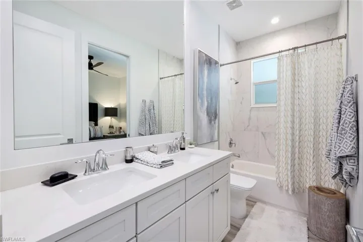 Full bathroom with shower / bath combo, vanity with extensive cabinet space, ceiling fan, toilet, and dual sinks