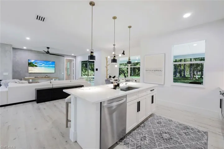 Kitchen featuring decorative light fixtures, an island with sink, stainless steel dishwasher, white cabinets, and sink