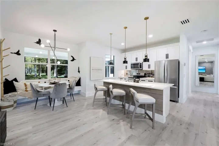 Kitchen with decorative light fixtures, white cabinets, light hardwood / wood-style flooring, a breakfast bar area, and appliances with stainless steel finishes