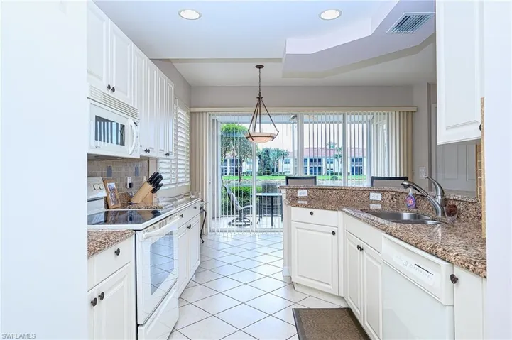Kitchen featuring white cabinetry, dark stone countertops, white appliances, and sink