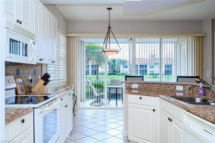Kitchen featuring pendant lighting, white cabinetry, light stone countertops, and white appliances
