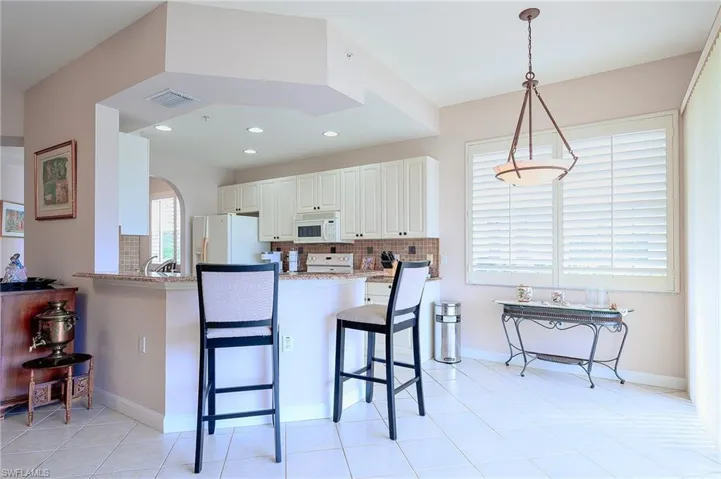 Kitchen featuring kitchen peninsula, light stone counters, white appliances, decorative light fixtures, and a breakfast bar area