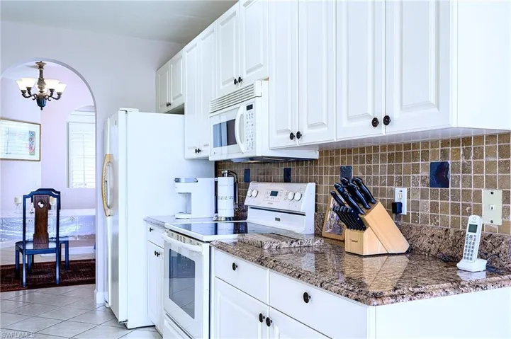 Kitchen with decorative backsplash, white cabinetry, light tile patterned floors, and white appliances