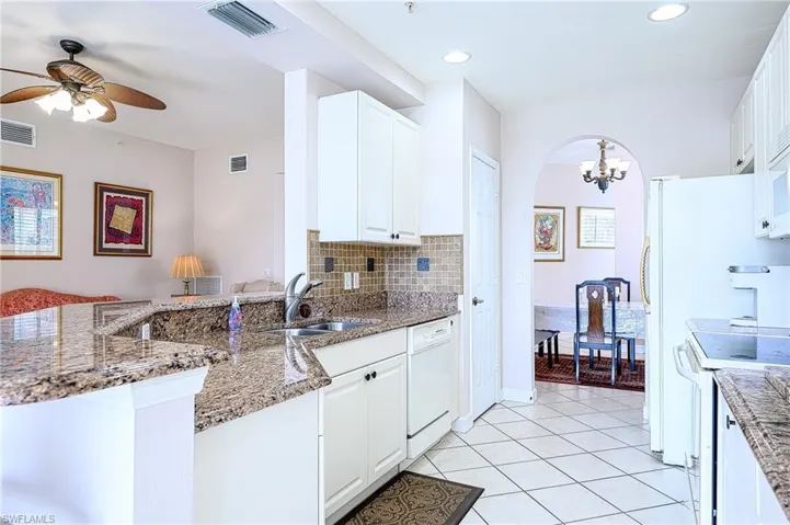 Kitchen featuring tasteful backsplash, kitchen peninsula, dark stone counters, white appliances, and white cabinets
