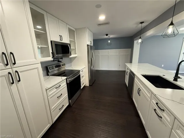 Kitchen featuring stainless steel appliances, white cabinets, light stone countertops, glass fronted cabinets, and dark wood-type flooring