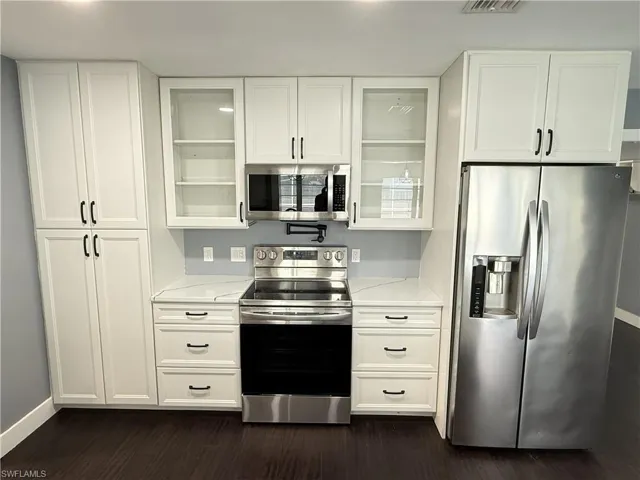 Kitchen featuring stainless steel appliances, white cabinets, light stone countertops, and dark wood-style floors