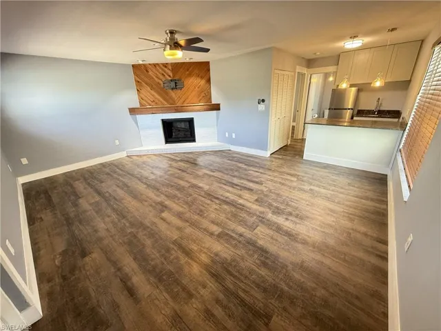 Guest House, Unfurnished living room with dark wood-type flooring, ceiling fan, and a fireplace with raised hearth