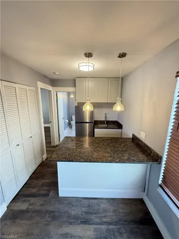 Guest House, Kitchen with a peninsula, dark wood-type flooring, freestanding refrigerator, white cabinets, and a breakfast bar area