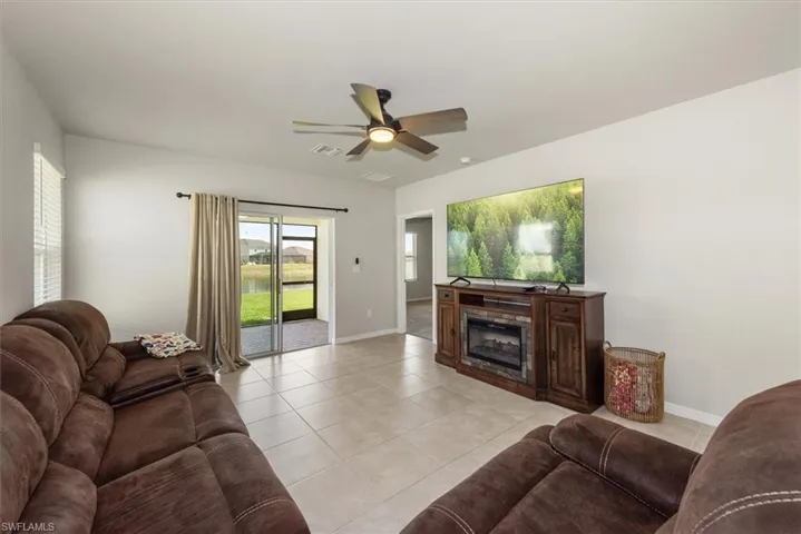 Living area with light tile patterned floors, a fireplace, a ceiling fan, visible vents, and baseboards