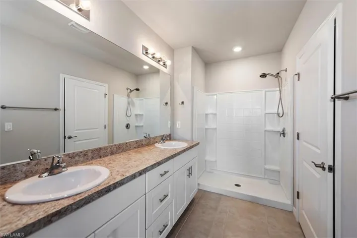 Bathroom featuring tile patterned flooring, double vanity, a tile shower, and a sink