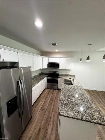 Modern kitchen featuring stainless steel appliances, white cabinetry, speckled countertops, wood-finish flooring, and recessed lighting