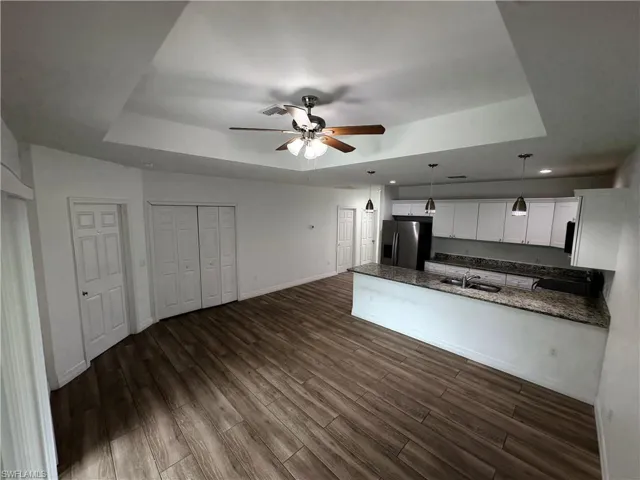 Tray ceiling with a ceiling fan, wood-finish flooring, kitchen island with a sink, stainless steel refrigerator, and pendant lighting