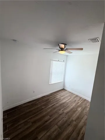 Wood-finish flooring, ceiling fan with integrated lighting, window with horizontal blinds, and clean white walls