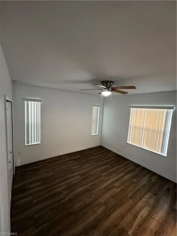 Wood-finish flooring throughout, ceiling fan with integrated lighting, two vertically oriented windows with blinds, one horizontally oriented window with blinds, and white painted walls