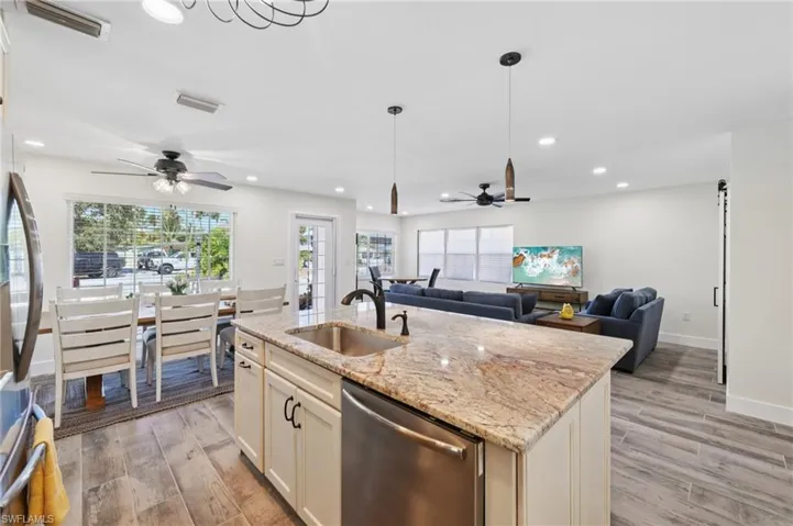 Kitchen with light stone counters, stainless steel appliances, light wood-style flooring, open floor plan, and ceiling fan