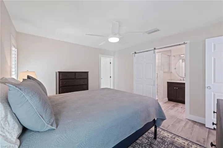 Bedroom with light wood-style floors, a barn door, ceiling fan, and ensuite bath