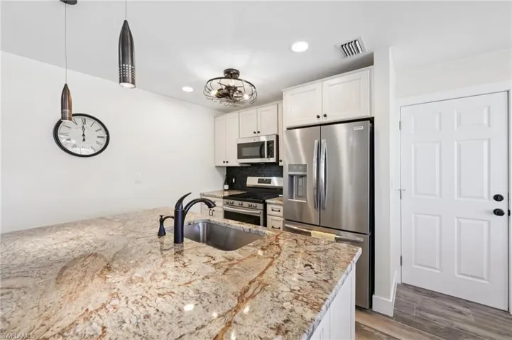 Kitchen featuring appliances with stainless steel finishes, white cabinetry, decorative backsplash, recessed lighting, and wood finished floors