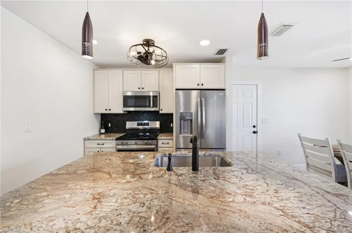 Kitchen featuring decorative backsplash, stainless steel appliances, hanging light fixtures, light stone countertops, and recessed lighting