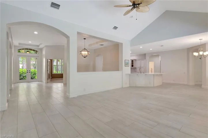 Unfurnished living room with sink, lofted ceiling, french doors, and ceiling fan with notable chandelier