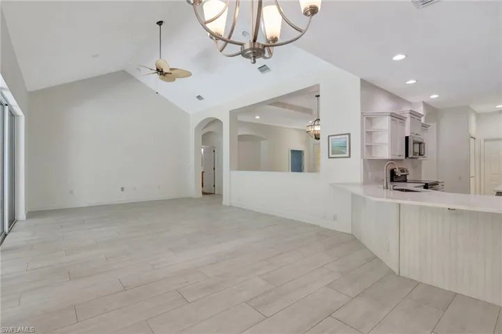 Unfurnished living room with high vaulted ceiling, ceiling fan with notable chandelier, and sink