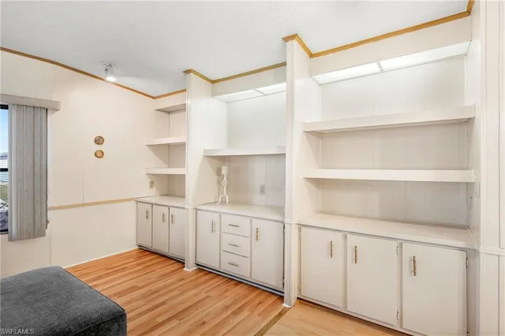 Kitchen with a textured ceiling, light countertops, crown molding, light wood finished floors, and open shelves