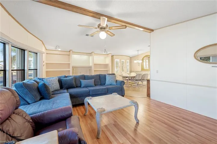 Living room featuring lofted ceiling with beams, visible vents, light wood-style flooring, and a healthy amount of sunlight