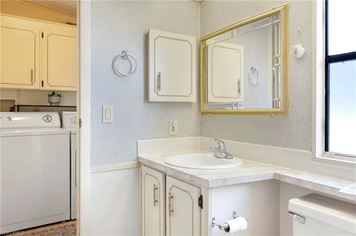 Bathroom featuring washing machine and clothes dryer, wallpapered walls, toilet, and vanity