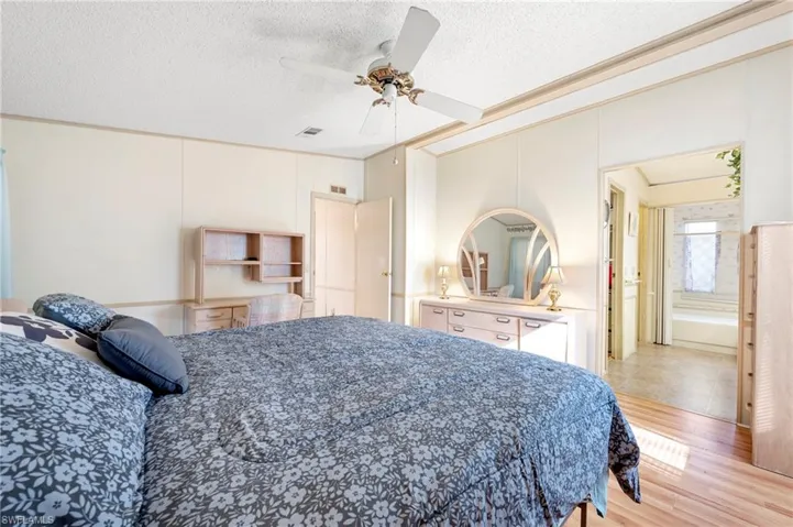 Bedroom with a textured ceiling, visible vents, light wood-style floors, and ceiling fan