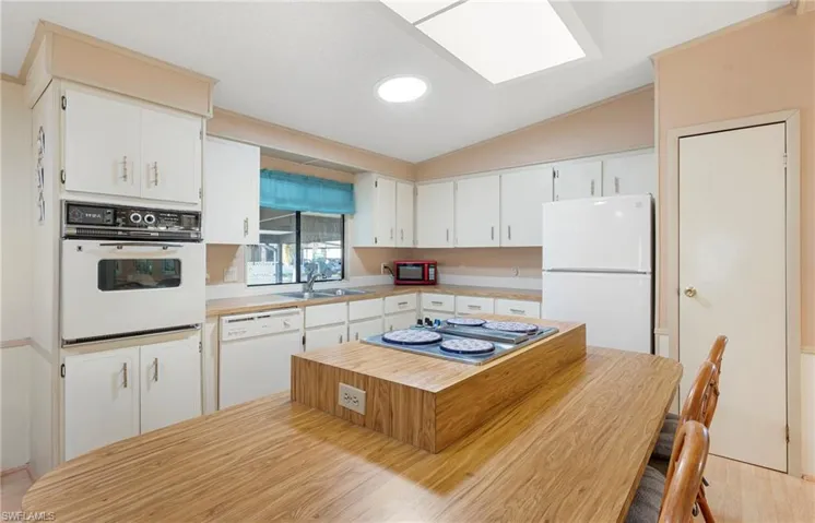 Kitchen with light countertops, lofted ceiling, white appliances, a sink, and white cabinets