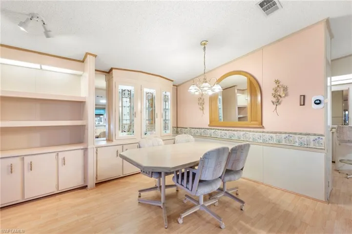 Dining space featuring light wood-type flooring, a chandelier, a textured ceiling, a wainscoted wall, and visible vents