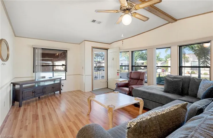 Living area with ornamental molding, lofted ceiling with beams, ceiling fan, light wood-style flooring, and visible vents