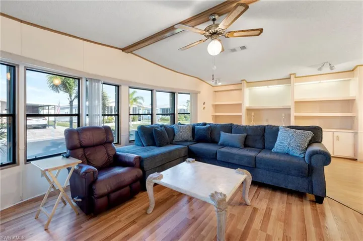 Living area with a textured ceiling, light wood finished floors, visible vents, a ceiling fan, and vaulted ceiling with beams