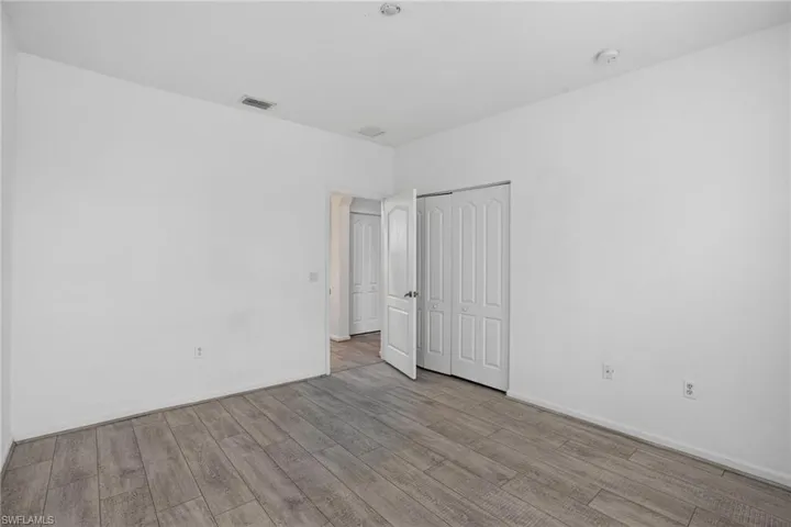 Spacious room featuring wood-finish flooring, white walls, and a ceiling-mounted smoke detector