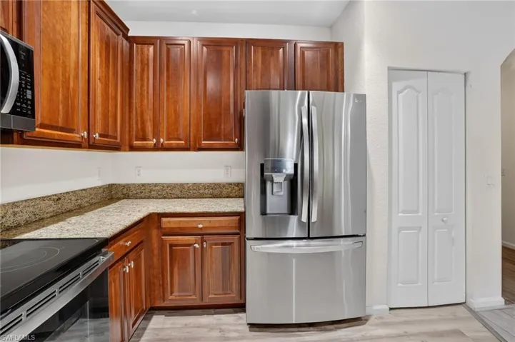 Kitchen featuring wood cabinetry, granite countertops, stainless steel refrigerator, black electric range, and wood-finish flooring