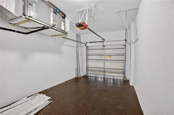 Garage featuring a roll-up door, automatic opener, textured white walls, and a concrete floor