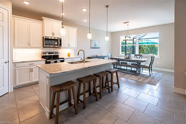 Kitchen with white cabinets, a kitchen island with sink, stainless steel appliances, a breakfast bar area, and backsplash