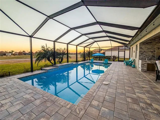 Pool at dusk with a sunroom, an outdoor pool, a patio area, a yard, and glass enclosure