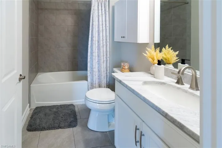 Full bathroom with vanity, shower / bath combo with shower curtain, and light tile patterned floors