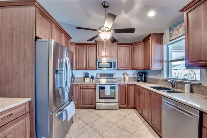 Kitchen featuring light tile patterned flooring, sink, ceiling fan, stainless steel appliances, and light stone countertops
