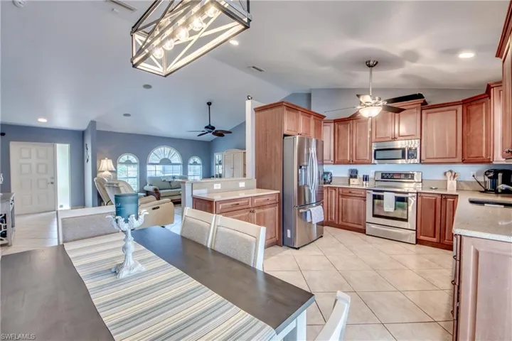 Kitchen featuring light tile patterned flooring, lofted ceiling, hanging light fixtures, ceiling fan, and stainless steel appliances