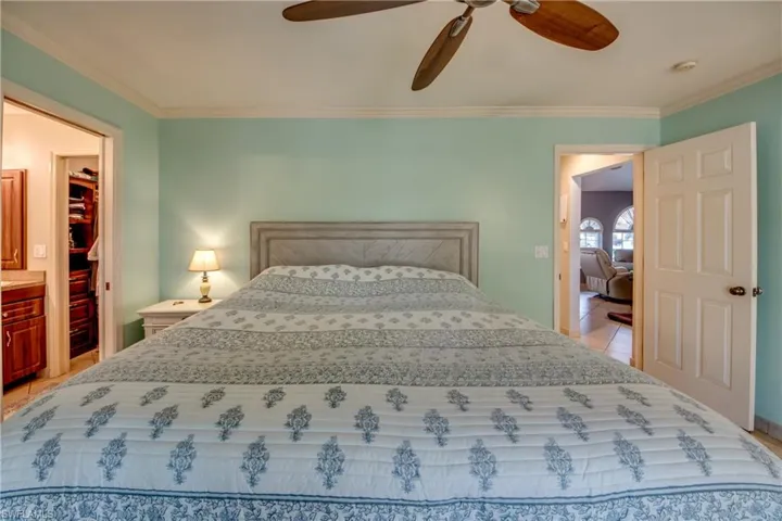 Bedroom featuring light tile patterned floors, a walk in closet, ornamental molding, and ceiling fan