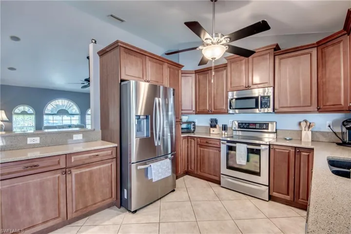 Kitchen featuring light stone counters, stainless steel appliances, ceiling fan, and light tile patterned flooring