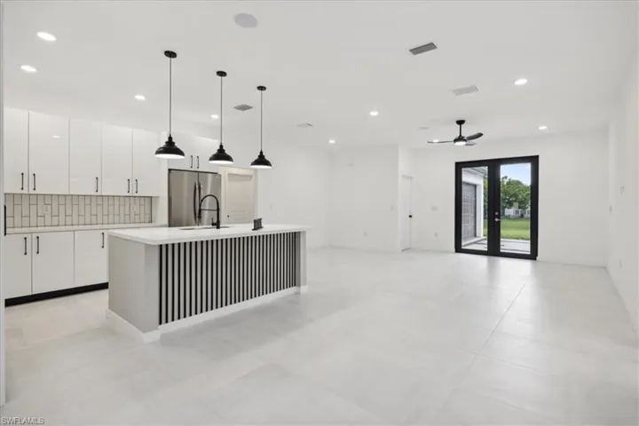 Kitchen featuring stainless steel fridge, decorative light fixtures, a center island with sink, white cabinetry, and ceiling fan