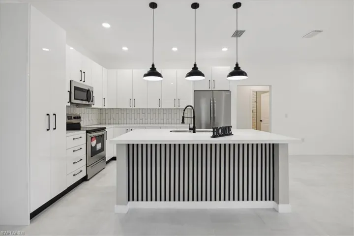 Kitchen with tasteful backsplash, decorative light fixtures, an island with sink, sink, and appliances with stainless steel finishes