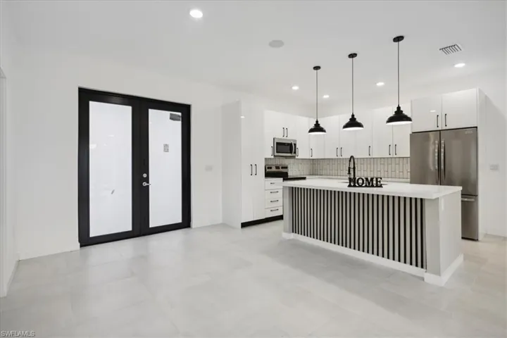 Kitchen with pendant lighting, backsplash, stainless steel appliances, a center island with sink, and white cabinets
